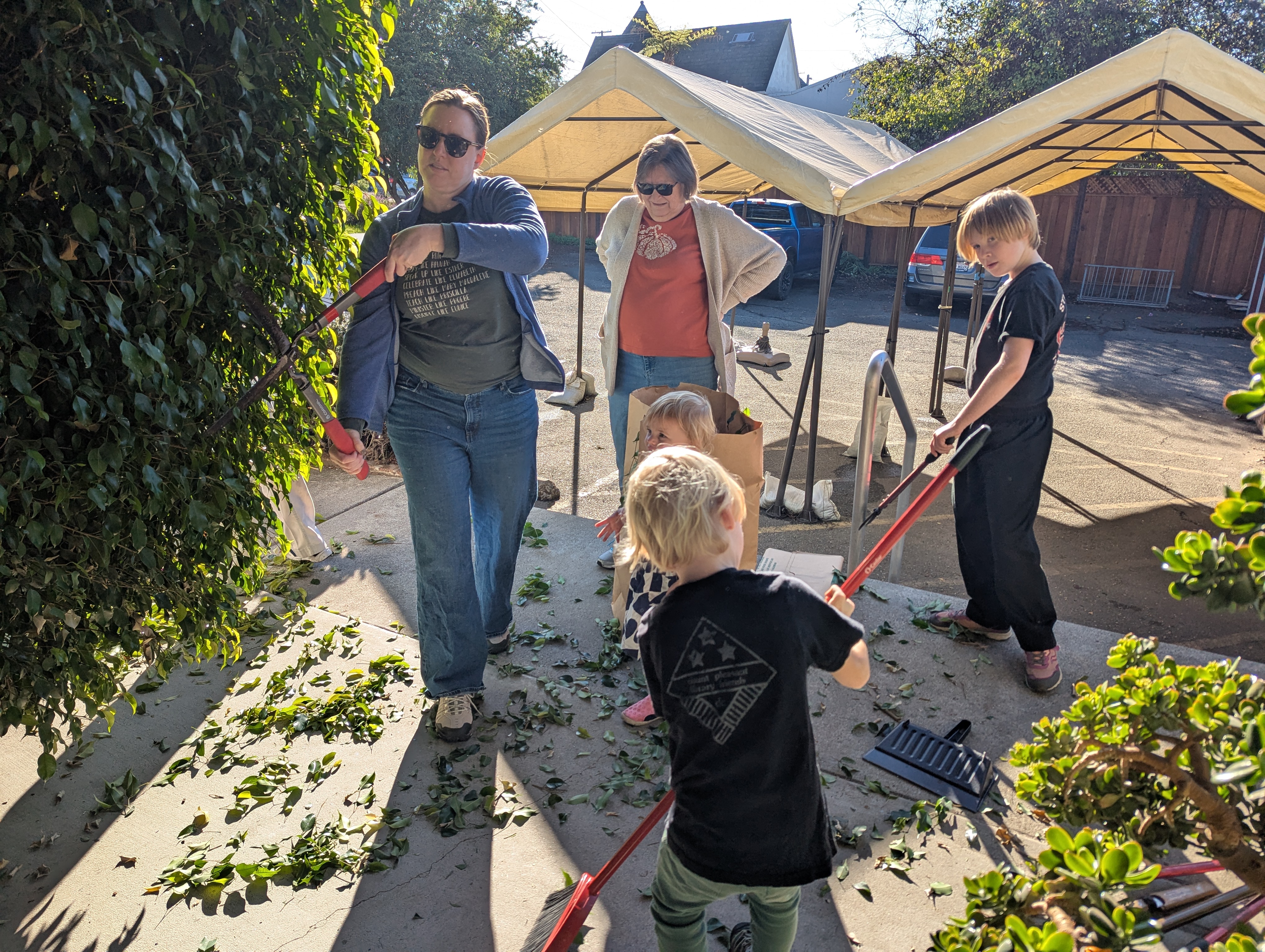 Community members of all ages working together outdoors, sweeping and tending the grounds