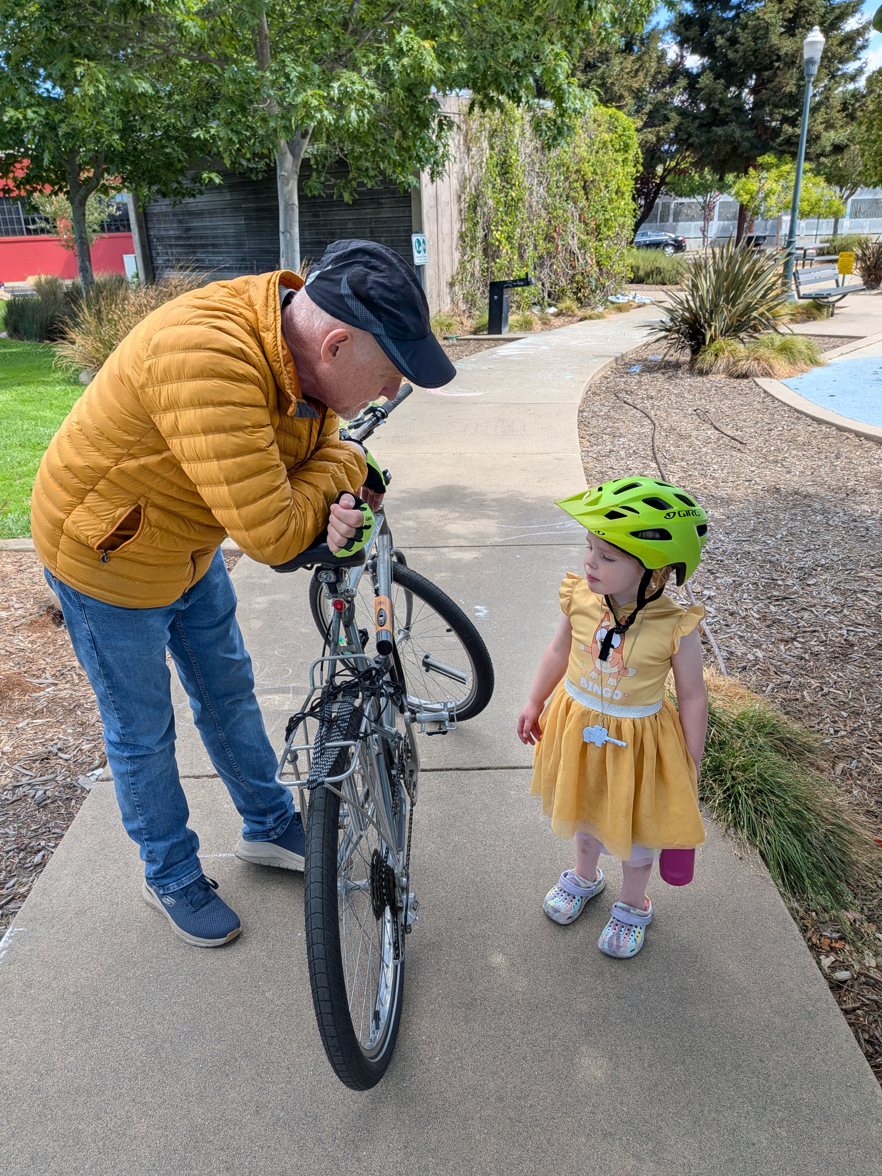 An elder helping a young child with a bicycle on a sunny day